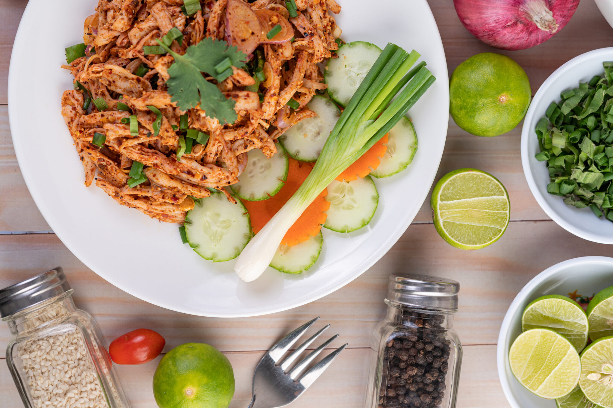 Spicy minced chicken on a white plate complete with cucumber, lettuce and side dishes on wooden table.